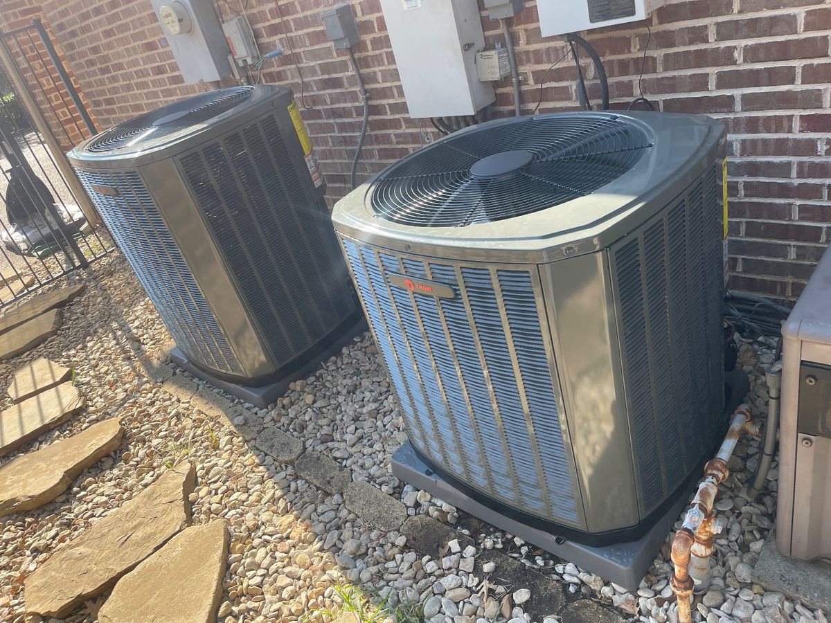 Two new Trane condensers on fresh pads beside a brick home